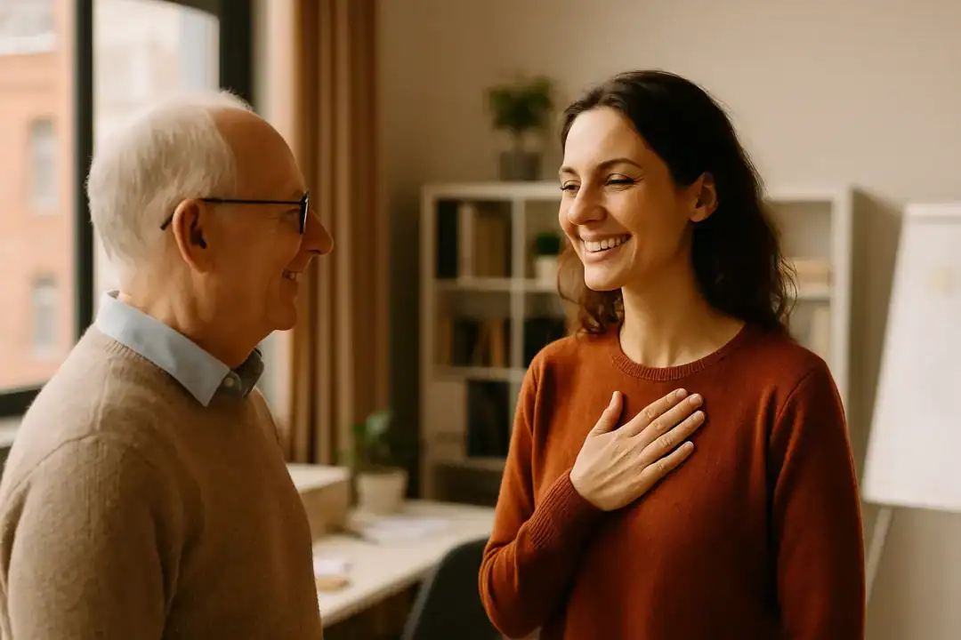 Mulher jovem sorrindo calorosamente para um homem mais velho em um ambiente de trabalho iluminado, simbolizando a espiritualidade expressa por meio de gestos de gentileza e presença.